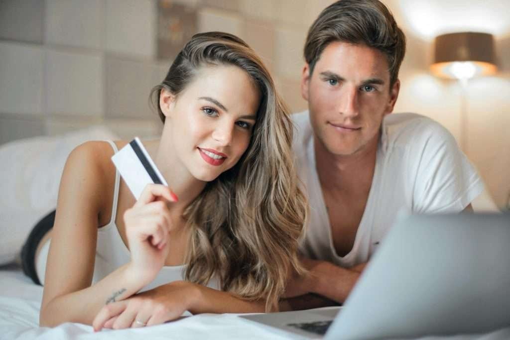 couple on bed holding card with laptop