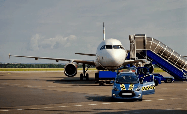 Airplane on tarmac with police vehicle and boarding stairs visible Aircraft parked on the tarmac with a police vehicle nearby and a boarding staircase in view