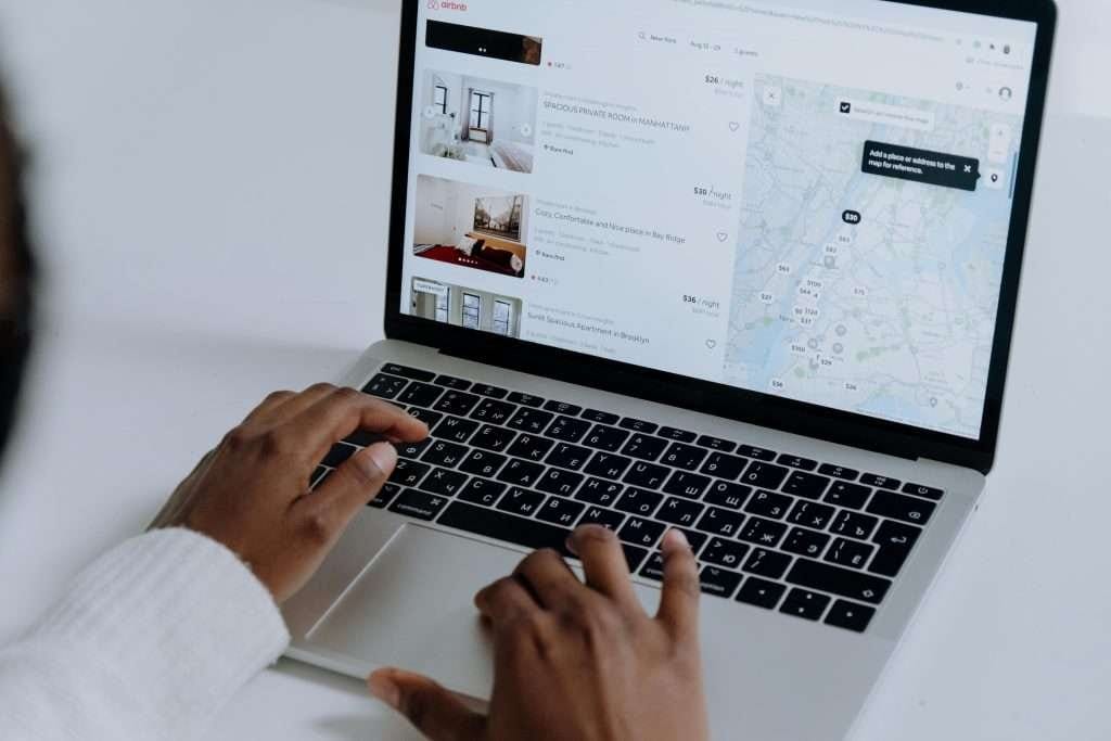 Person browsing Airbnb listings on a laptop, showing property options and a map for reference.
