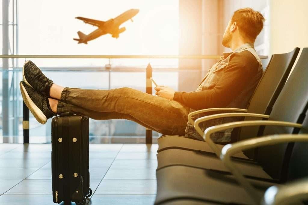 man at airport with legs on carryon luggage