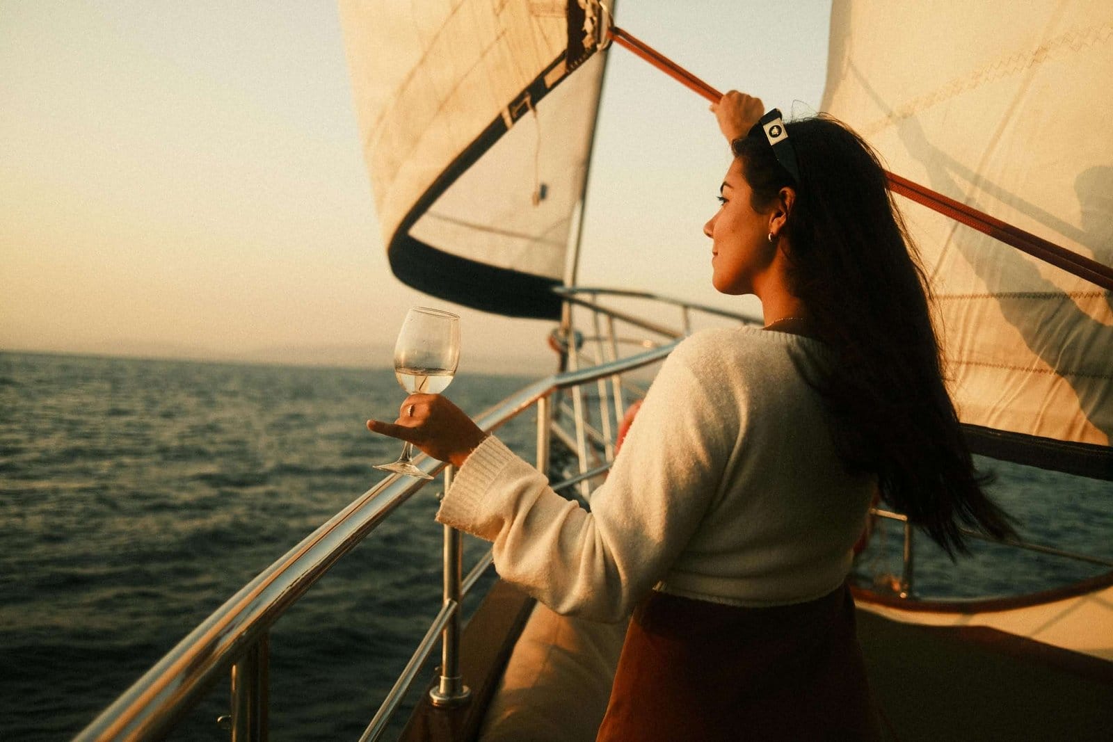 Woman relaxing on a sailboat at sunset. Woman holding a glass on a sailboat, enjoying the ocean and sunset.